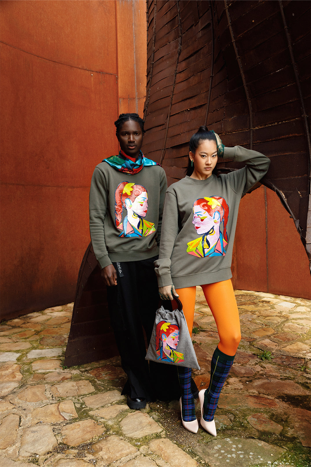 Unisex oversized green sweatshirt worn by two models, featuring a hand-crafted raised silicone abstract geometric face print, creating a three-dimensional and tactile effect.