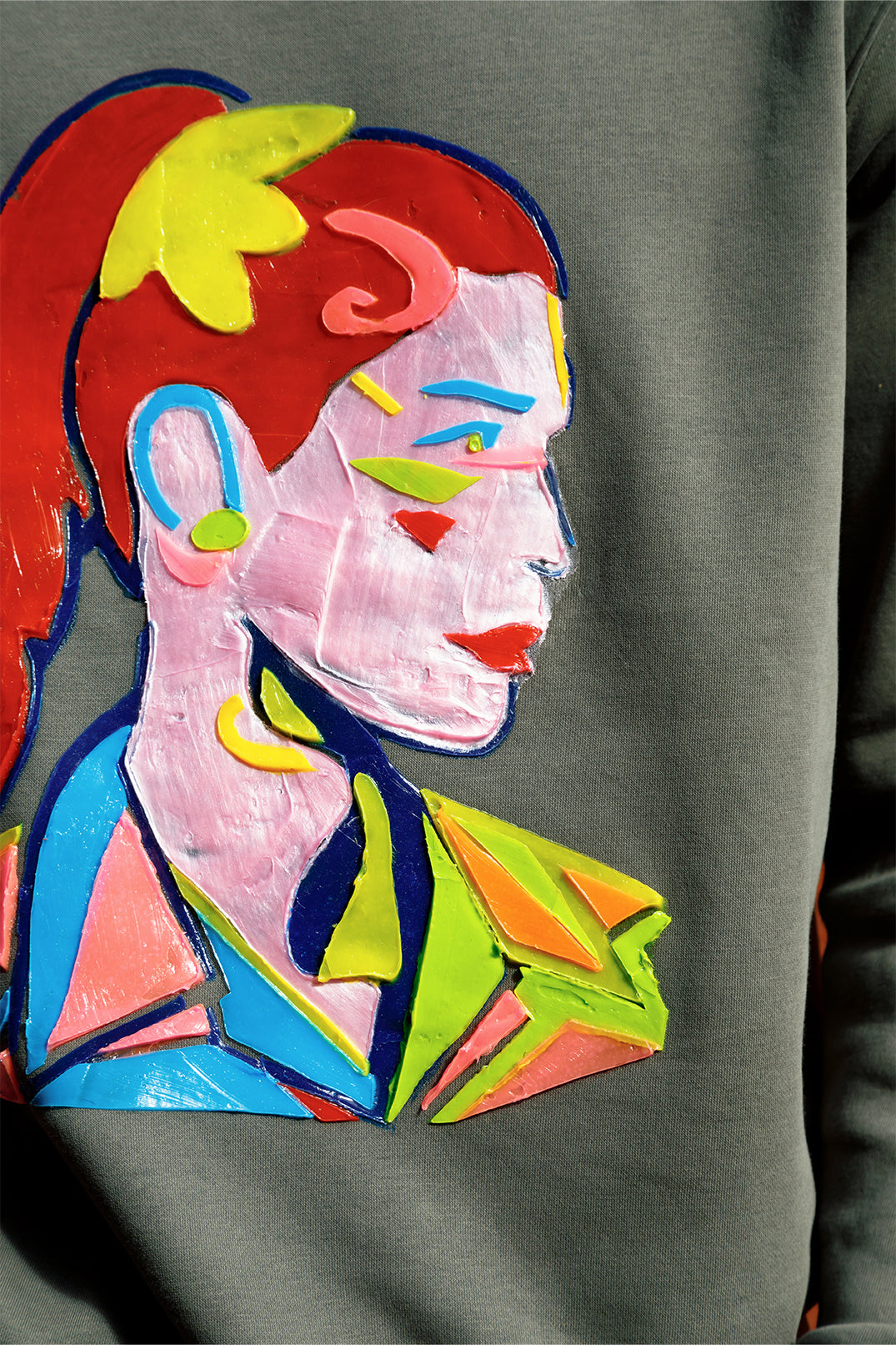 Close-up of the raised silicone abstract face print on the oversized green unisex sweatshirt, showcasing vibrant colors and tactile 3D texture.
