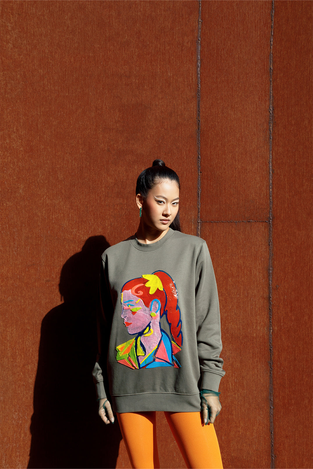 Unisex oversized green sweatshirt worn by a model, featuring a hand-crafted raised silicone abstract geometric face print, creating a three-dimensional and tactile effect.