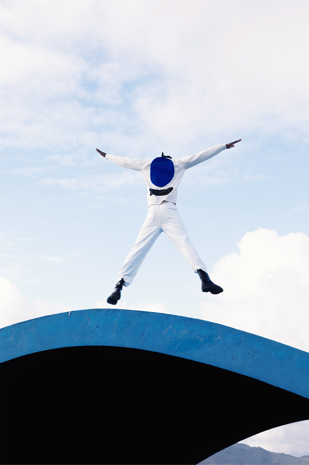 Back of the white sweatshirt worn by a model, with a large soft blue faux fur circle and a lower strip of black sequins reflecting light