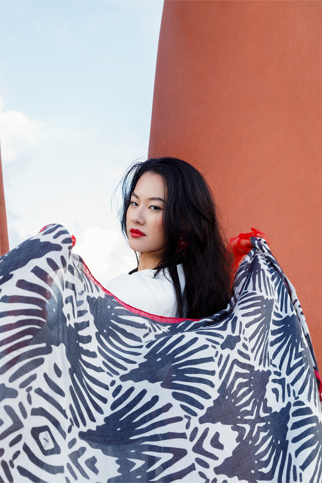 Scarf 70×180 cm in modal-cashmere blend with black and white fan motif, red border held by a model.