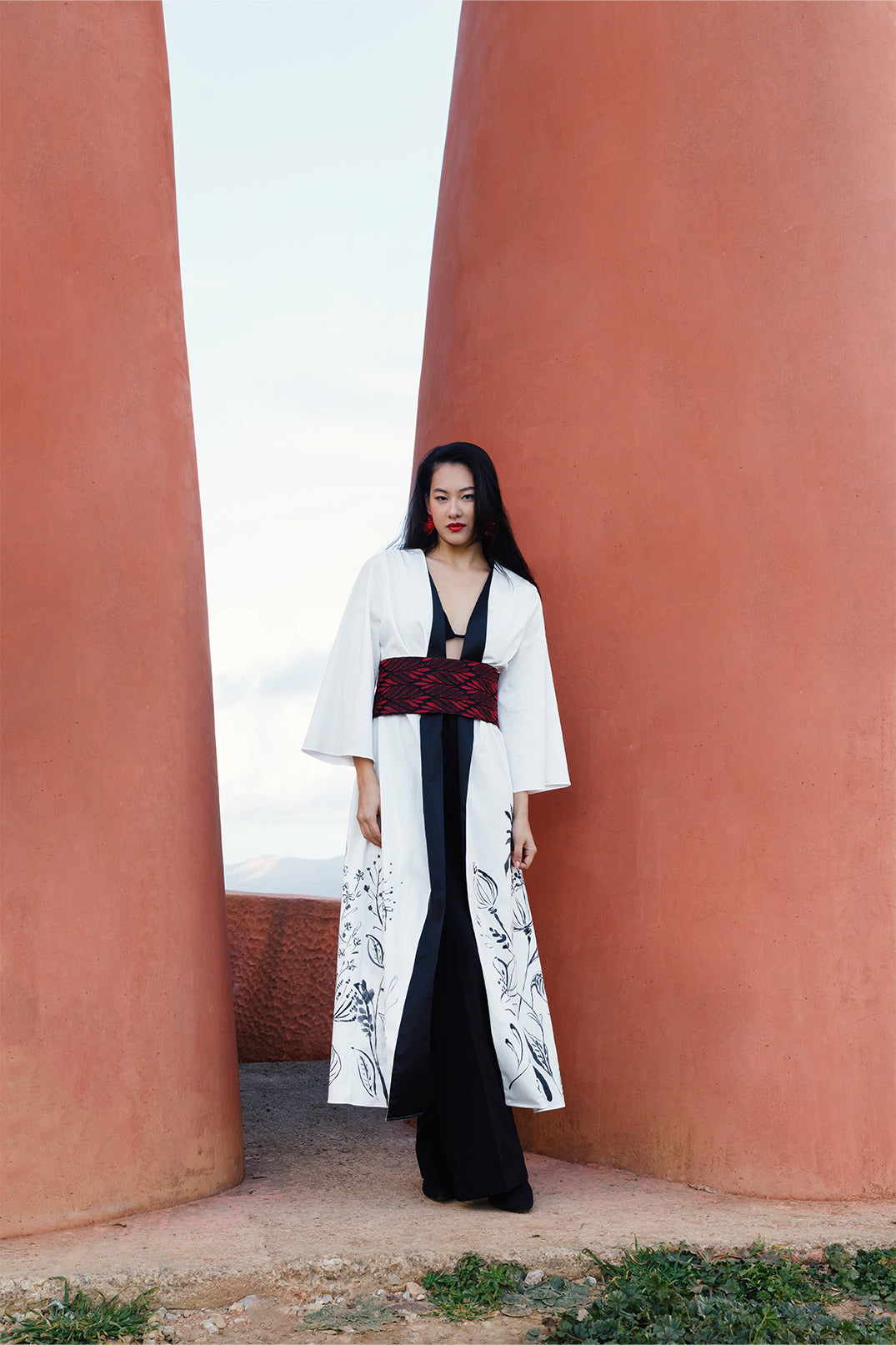 White long stretch cotton kimono worn by a model, featuring elegant hand-painted floral illustration directly on the fabric, with a brocade belt at the waist for a fluid and sophisticated silhouette.