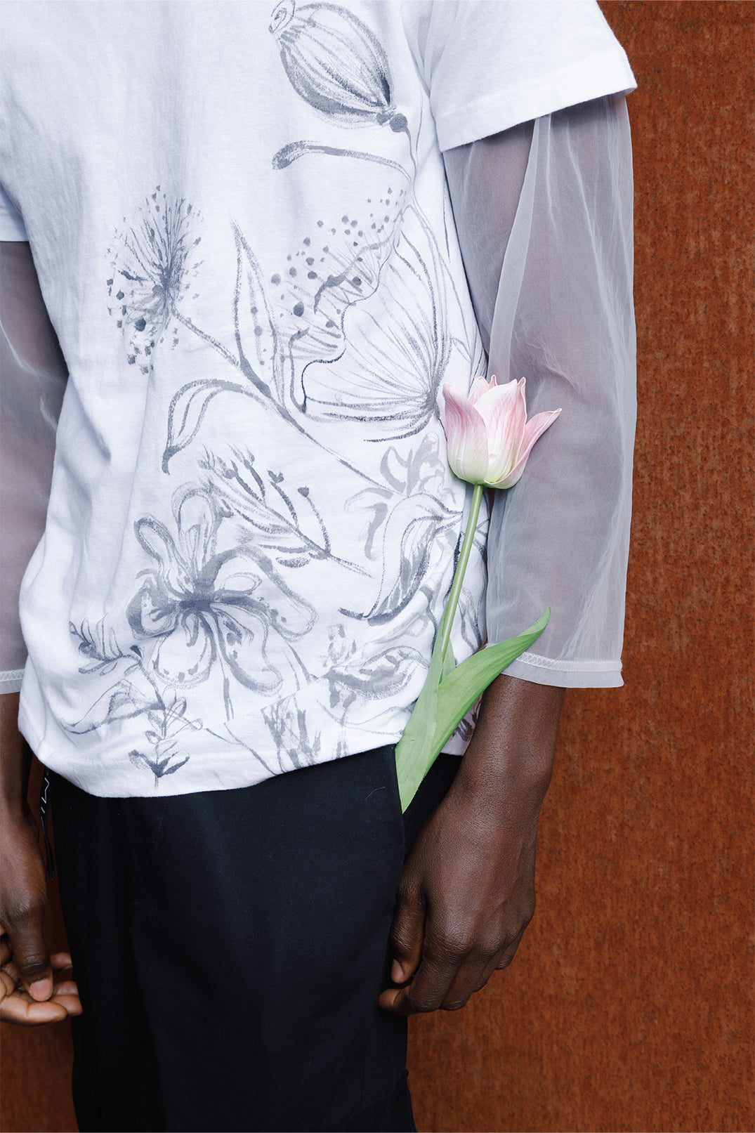 Close-up of the white unisex oversized T-shirt worn by a model, featuring hand-painted black flowers decorating the entire left side of the garment.