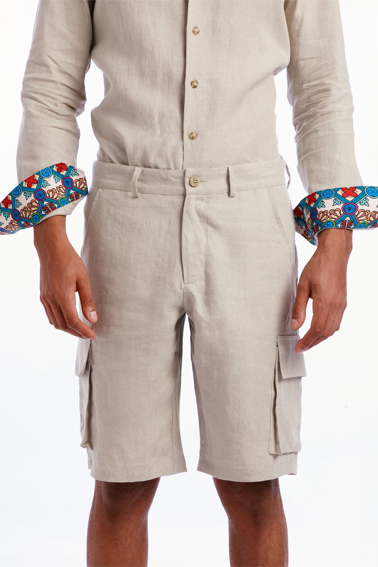 Close-up of the inner Sicilian majolica-inspired pattern on the cuffs of the linen shirt, showing intricate geometric and floral motifs. Beige linen cargo bermuda shorts featuring side patch pockets, breathable and exclusive pattern details on the back welt pockets and inner borders. Worn by a model.