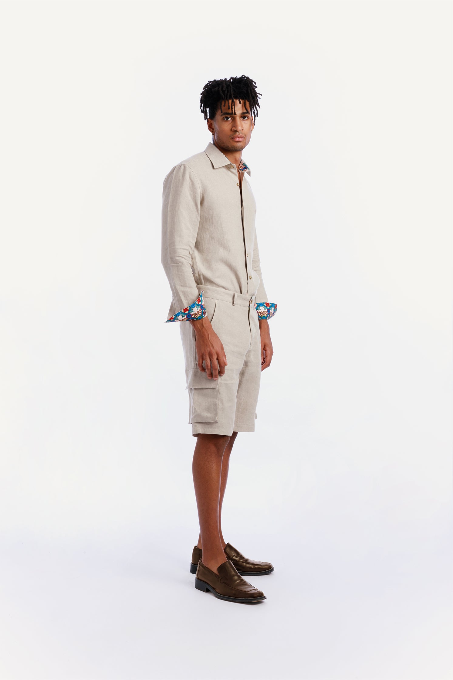 Side view of the beige linen cargo bermuda shorts worn by a model, featuring side patch pockets, breathable and exclusive pattern details on the back welt pockets and inner borders.