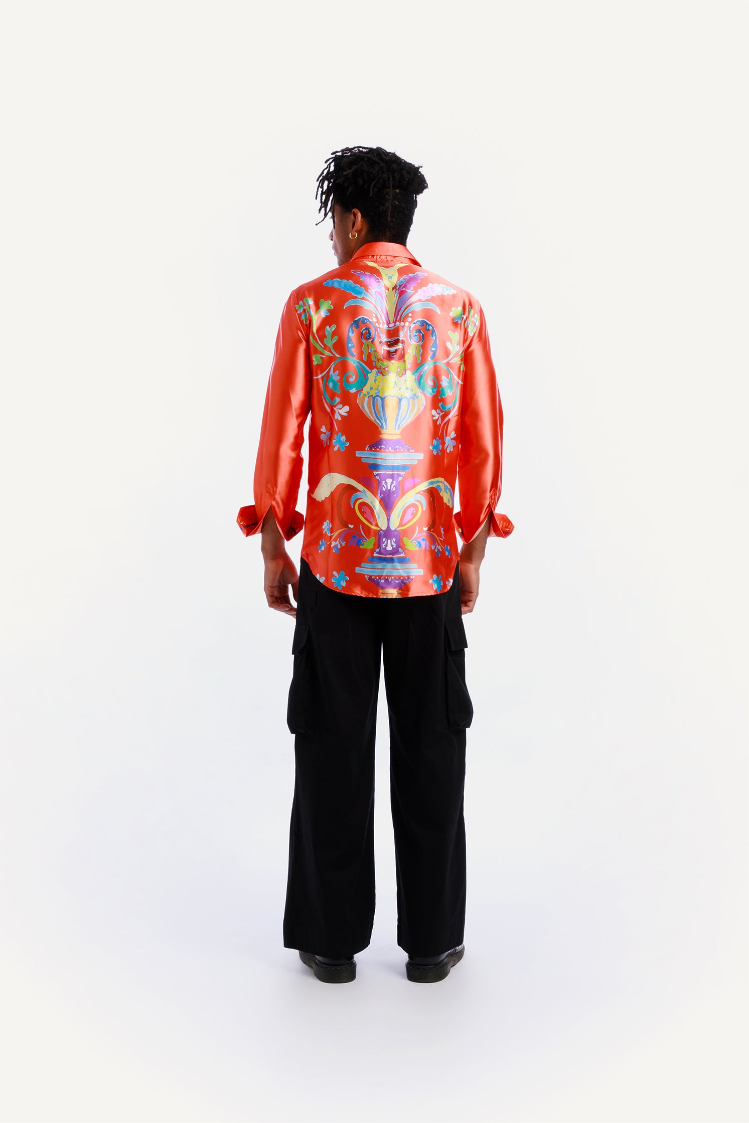 Back view of the long-sleeved shirt made of soft and shiny fabric, worn by a model, featuring an exclusive pattern on the back with a red-orange background and turquoise embroidery on the heart side.