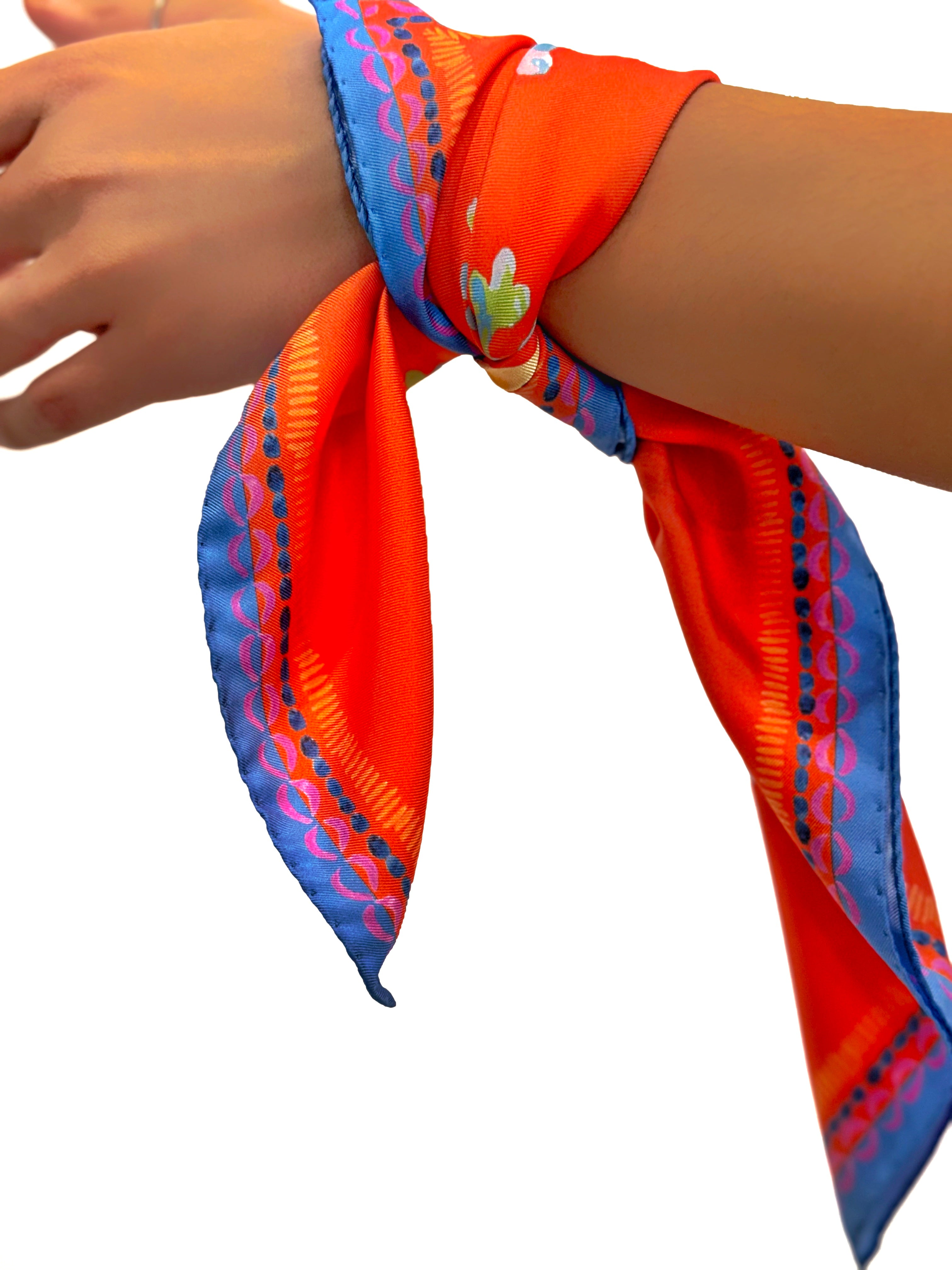 Square scarf 45x45 cm made of pure silk, featuring a surreal stylized painting called "Vaso" on a red-orange background worn around the wrist.