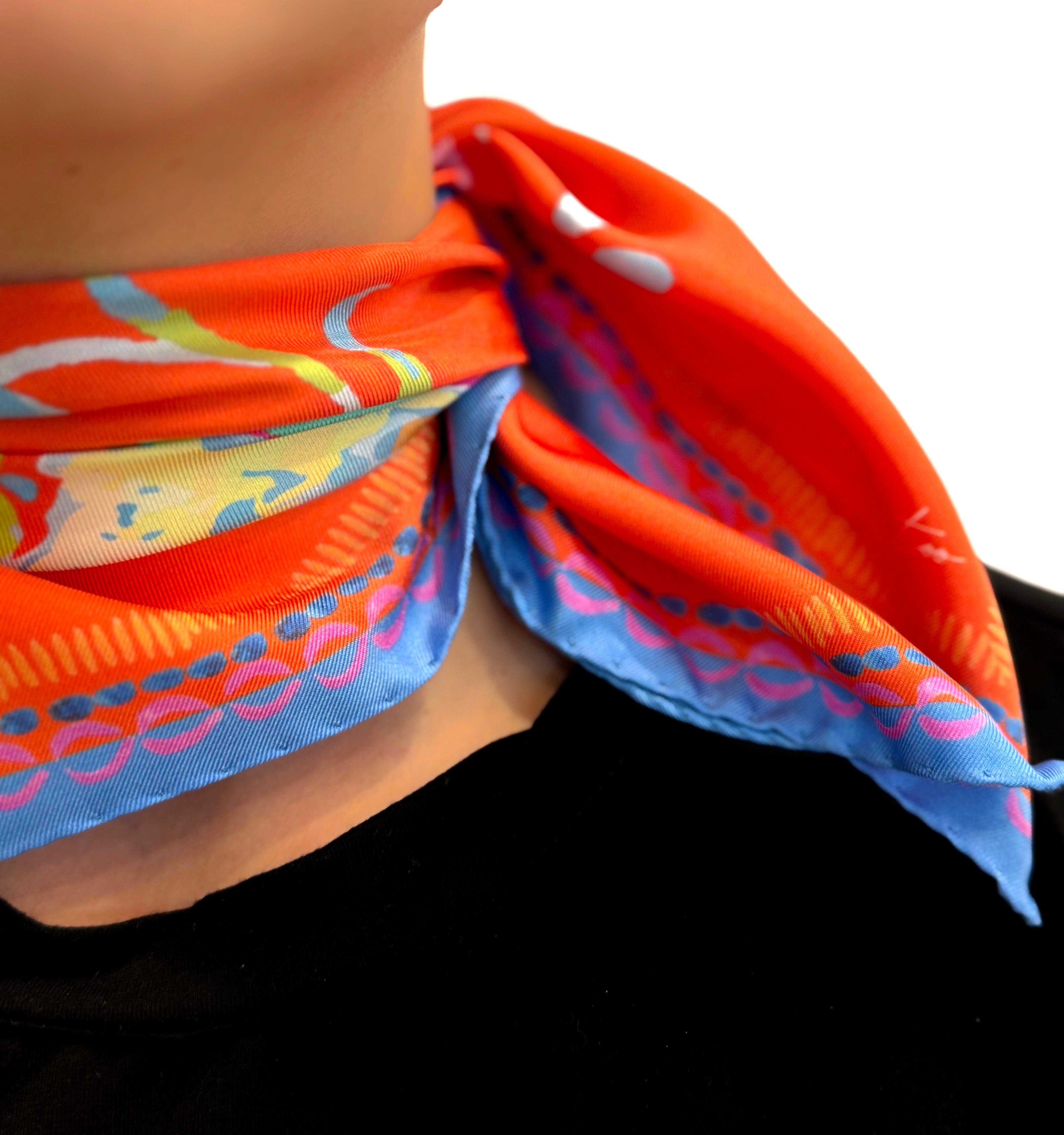 Square scarf 45x45 cm made of pure silk, featuring a surreal stylized painting called "Vaso" on a red-orange background worn around the neck.