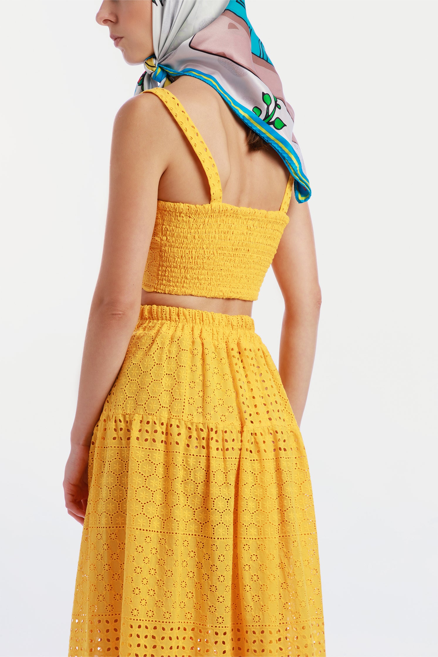 Back view of the pure silk scarf 90x90 cm worn around the head by a model, featuring a vibrant illustration of a Vespa in a colorful Sicilian landscape.