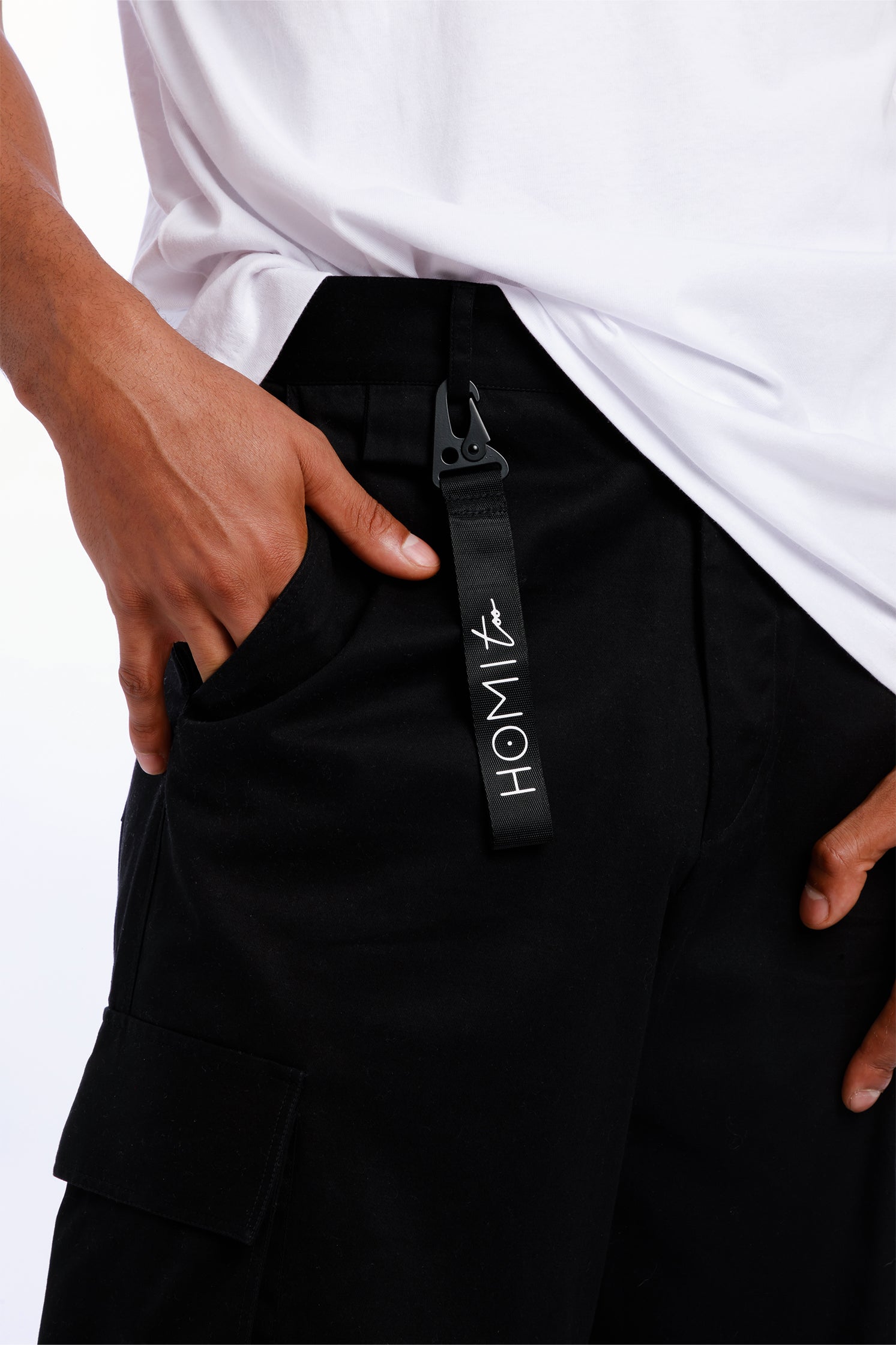 Close-up of the "Homi Too" logo on the black keychain, showing precise lettering and quality craftsmanship.