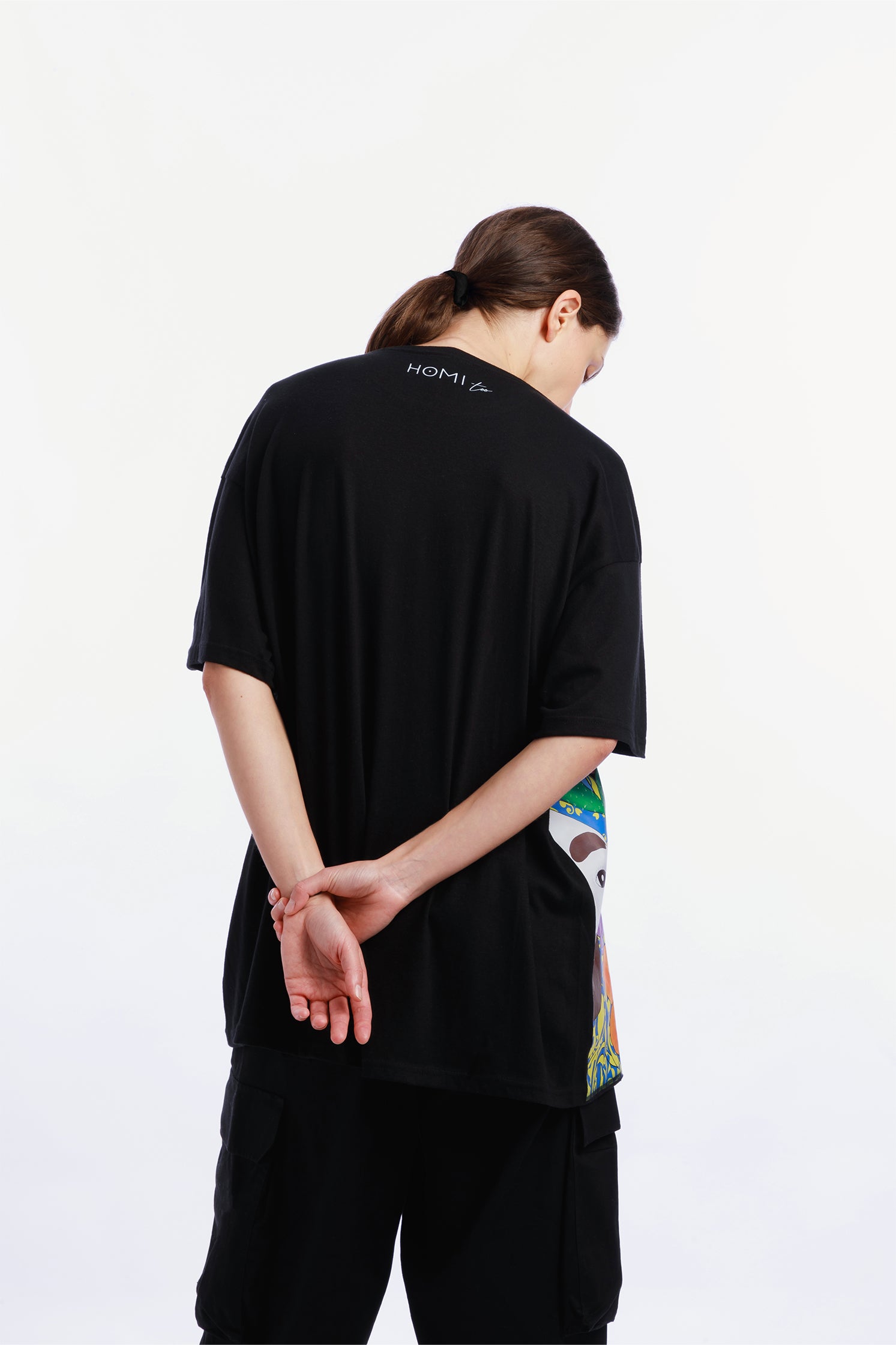 Back view of the black oversized unisex T-shirt made of 100% high-quality cotton, worn by a model, featuring the "Homi Too" logo printed on the collar.