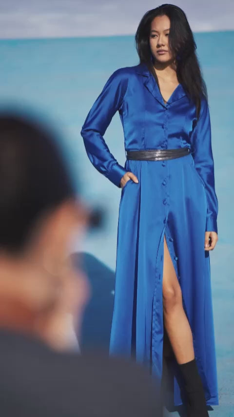 Elegant long royal blue dress worn by a model, with fluid silhouette, shirt collar, long sleeves