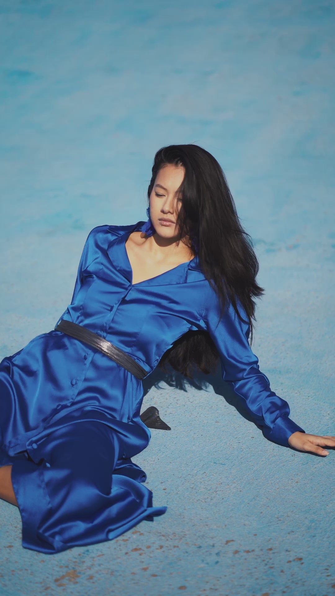 Elegant long royal blue dress worn by a model, with fluid silhouette, shirt collar, long sleeves