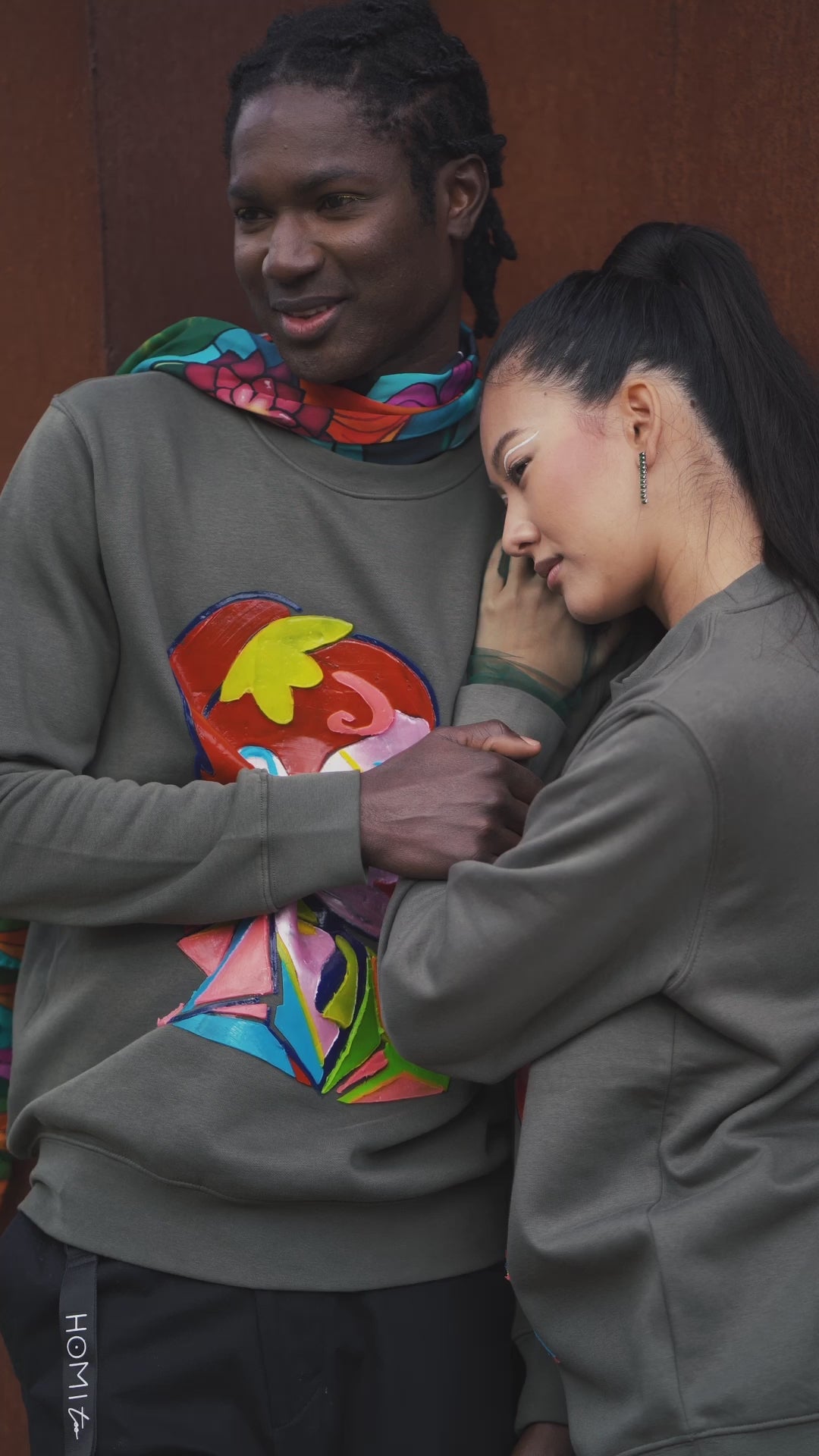 Unisex oversized green sweatshirt worn by two models, featuring a hand-crafted raised silicone abstract geometric face print, creating a three-dimensional and tactile effect