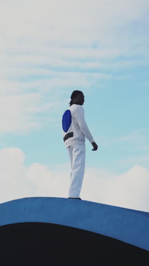 Back of the white sweatshirt worn by a model, with a large soft blue faux fur circle and a lower strip of black sequins reflecting light